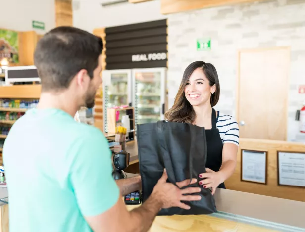 confident-female-cashier-giving-bag-young-man-checkout-counter-supermarket